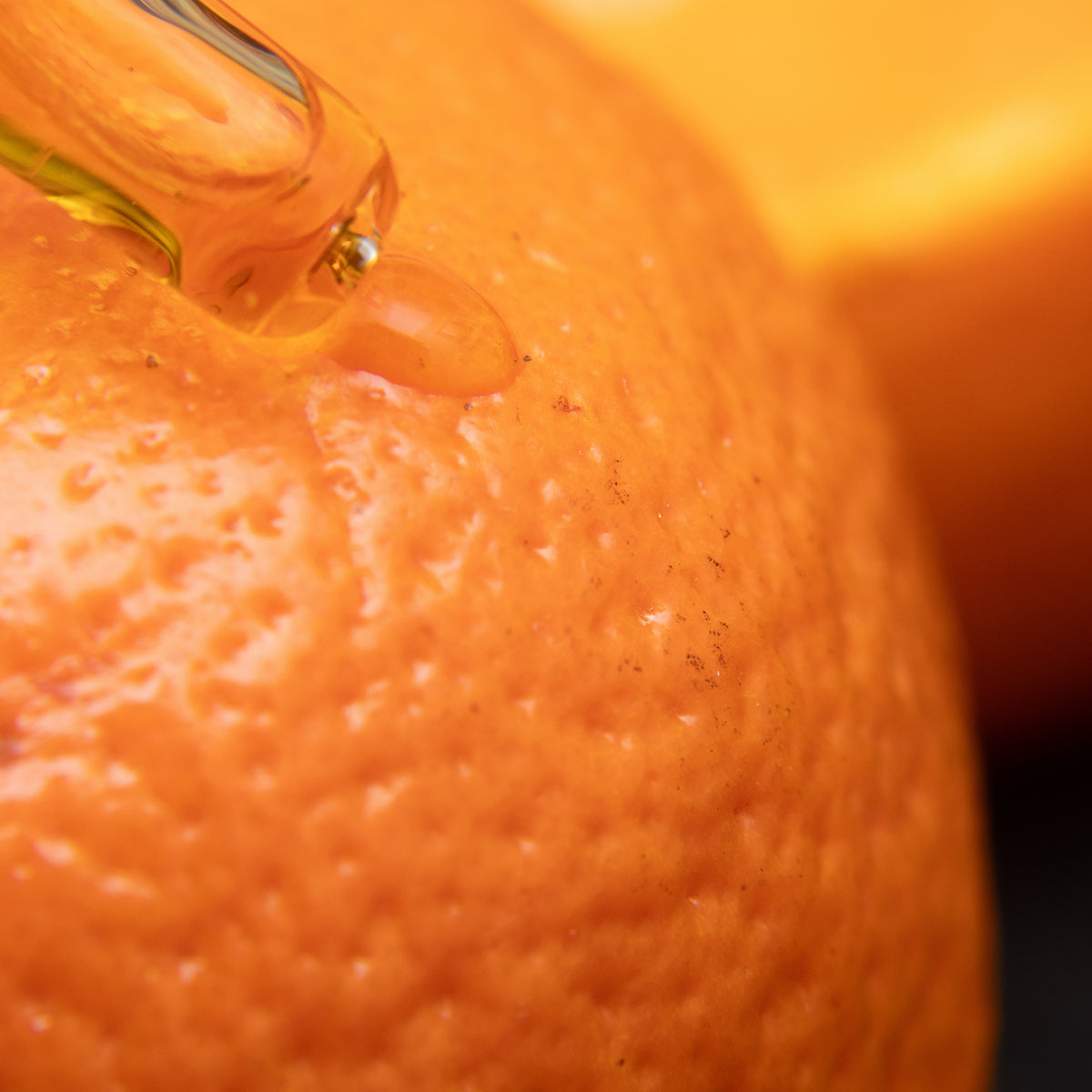 A droplet of vitamin C serum resting on the skin of a fresh orange