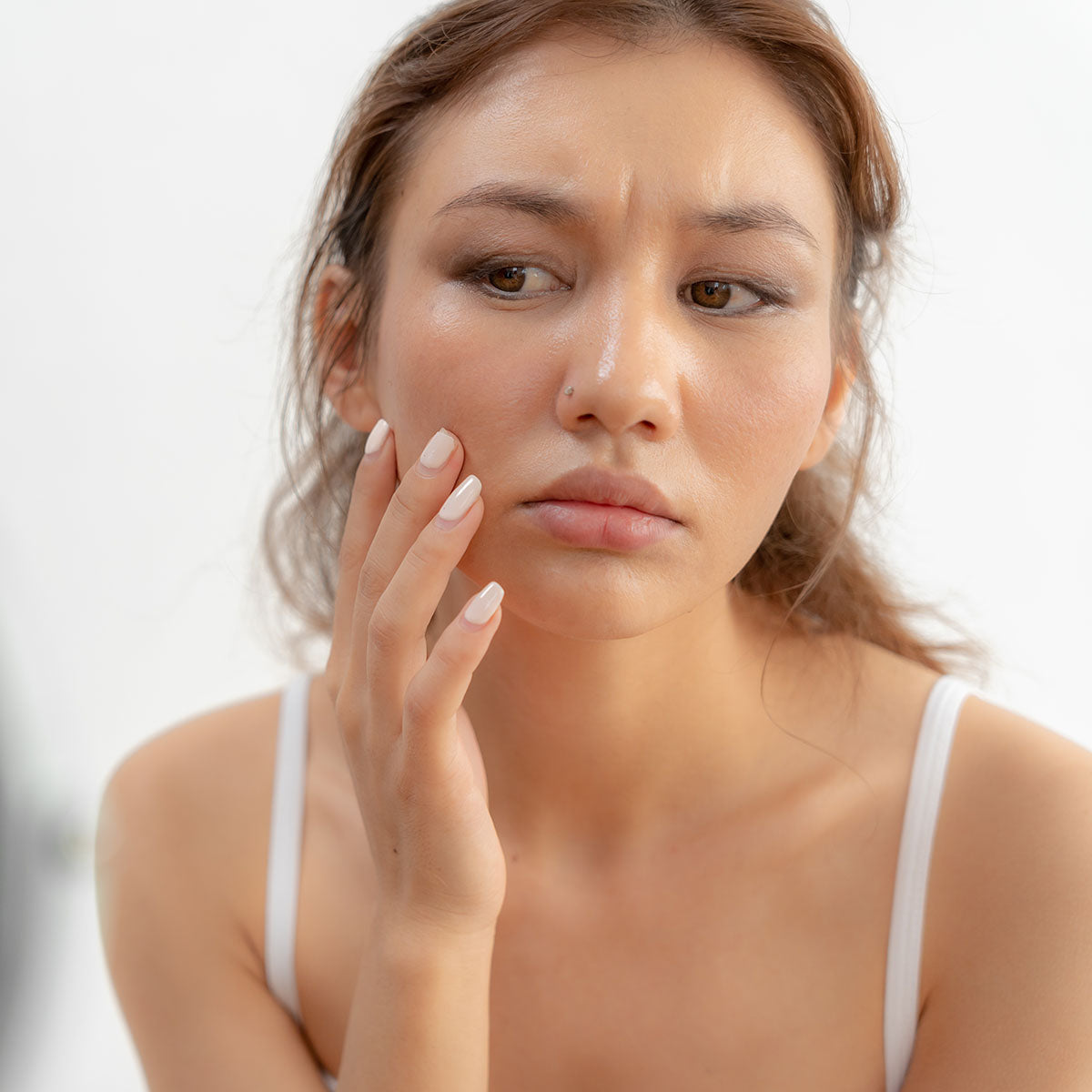Woman touching her reactive cheek in front of a mirror
