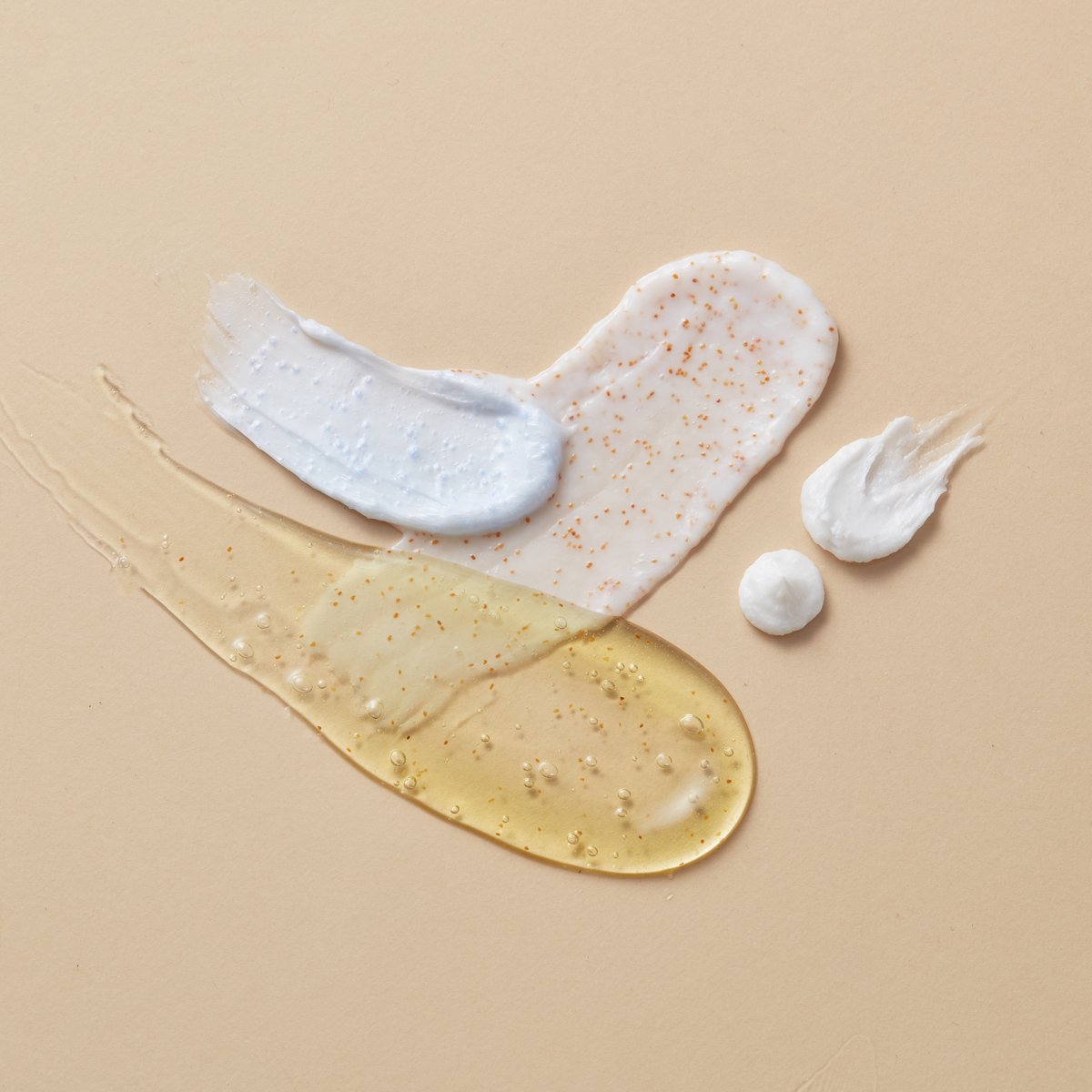 Swatches of cleanser, serum, oil and cream on a beige background, layered lightest to richest