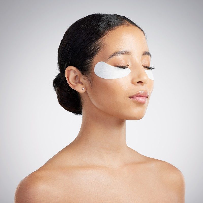 Woman resting with an under-eye patch, eyes closed, calm morning skincare moment