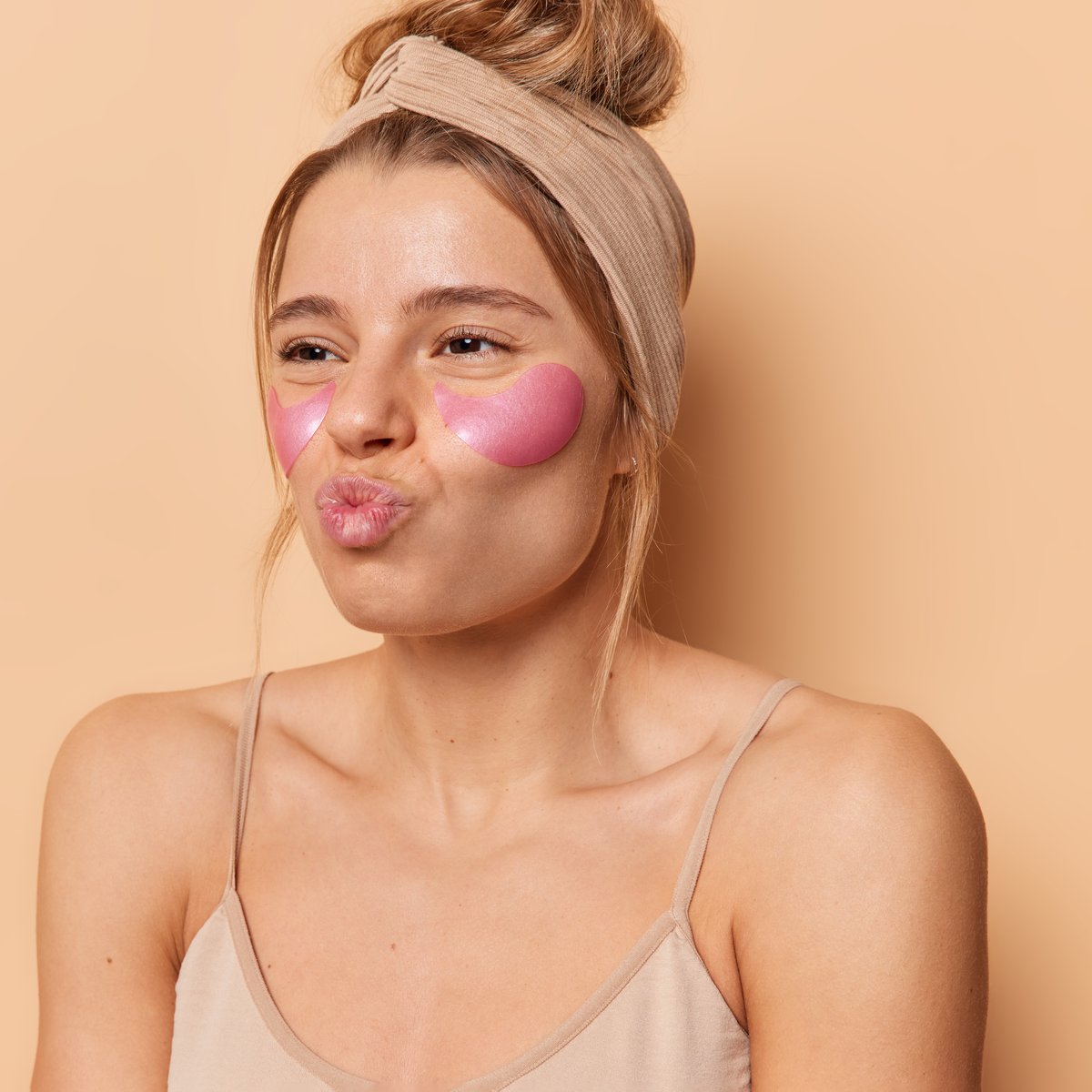 Relaxed woman in her early 30s wearing pink under-eye patches and a headband