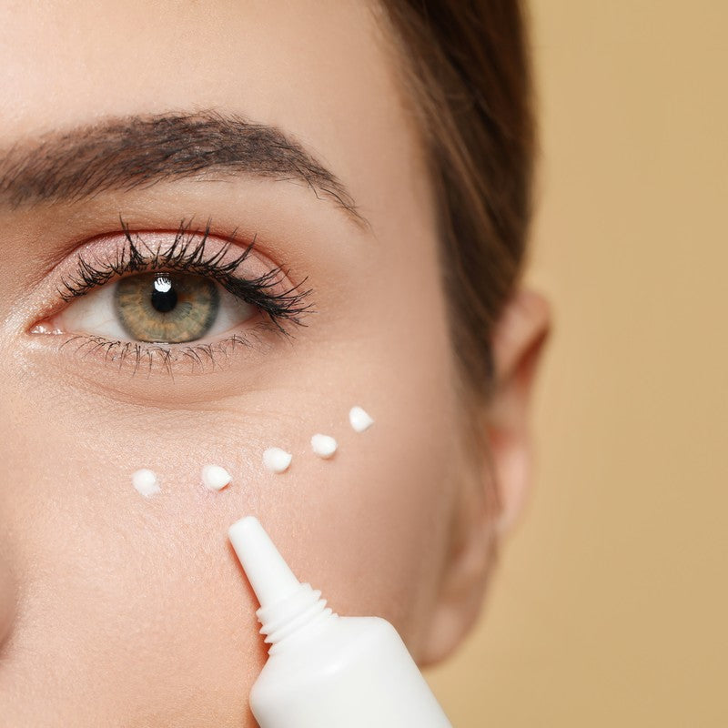 Close-up of a woman applying eye cream under her eye in soft natural light